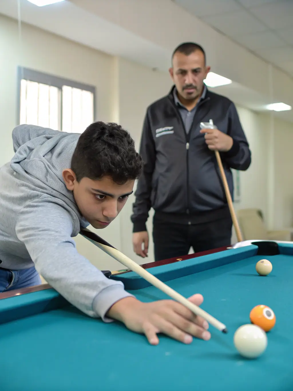 A close-up of a billiards instructor guiding a student on proper stance and grip techniques at UNION BILLARD CLUB ROCHEFORT.